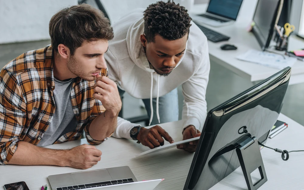 Two security engineers studying a monitor together in a bright office