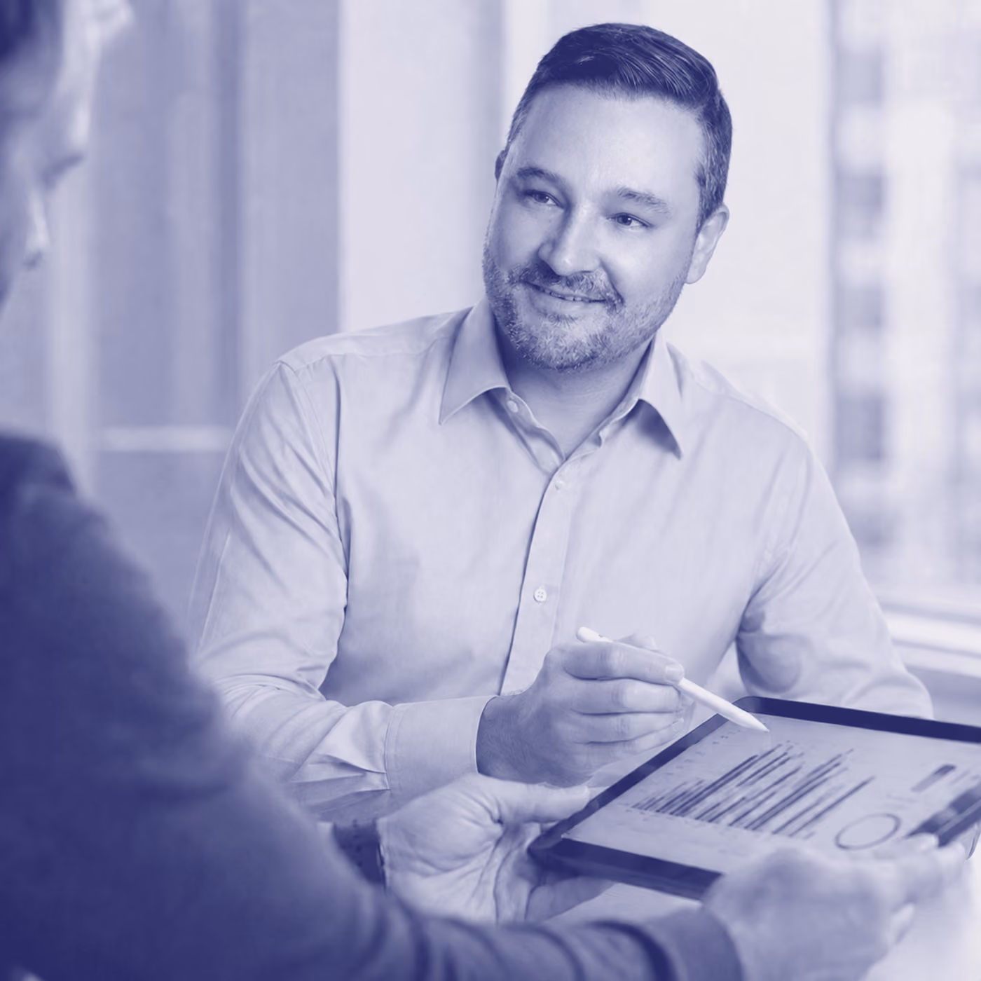Smiling man with a beard reviews charts on a tablet with a colleague, in blue duotone