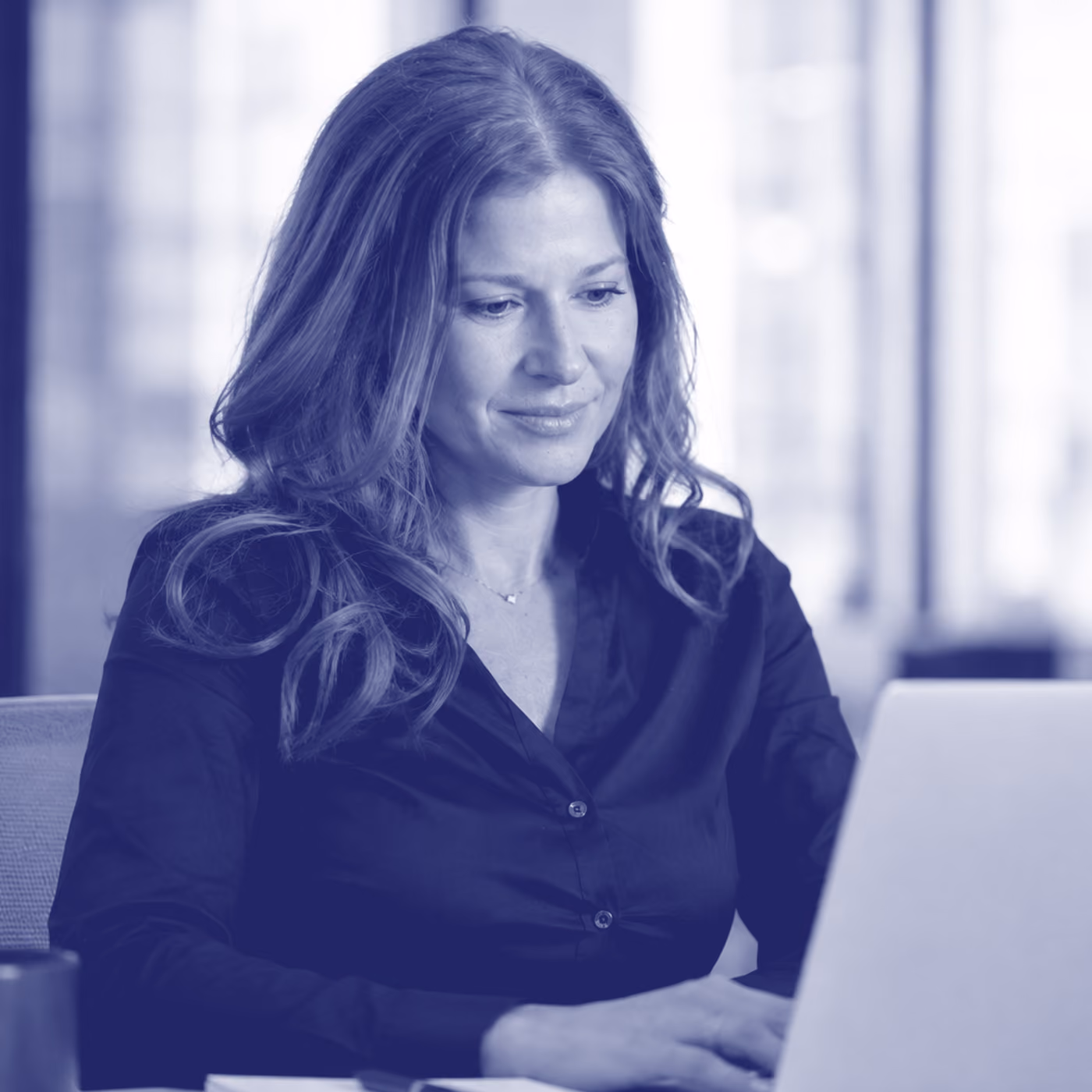 Jessica Cohen works at a laptop in a bright office, in blue duotone