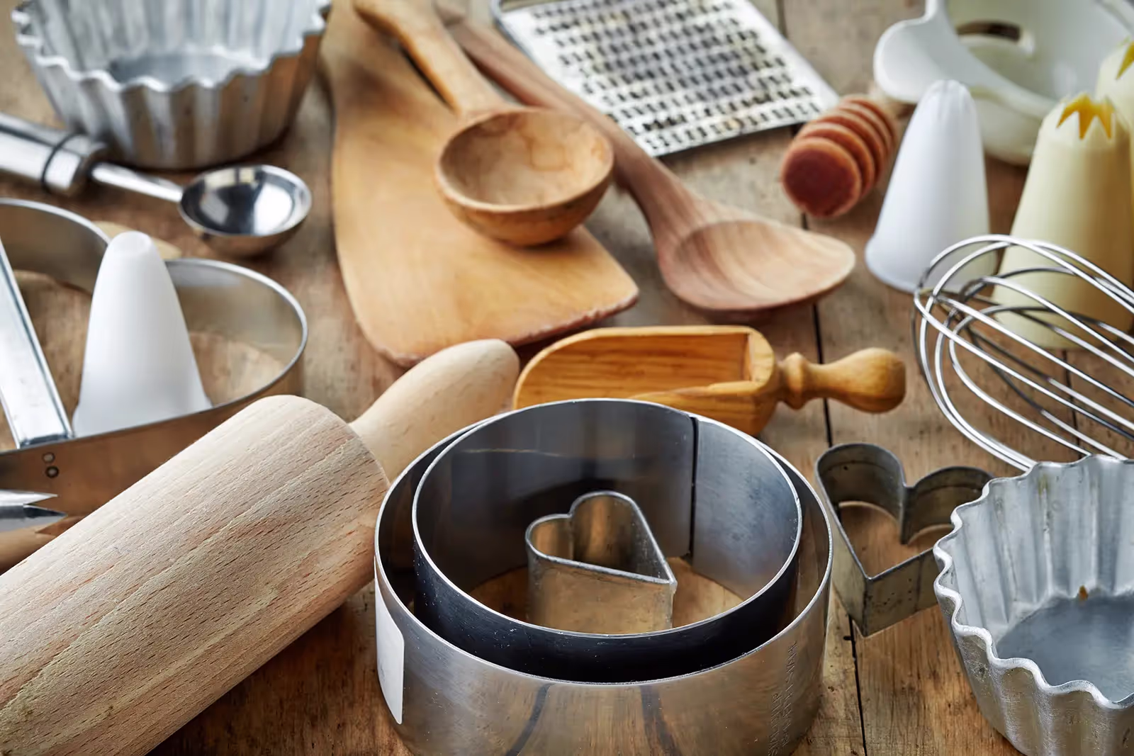 A close-up, high-angle shot of various baking tools and kitchen utensils scattered across a rustic wooden table.