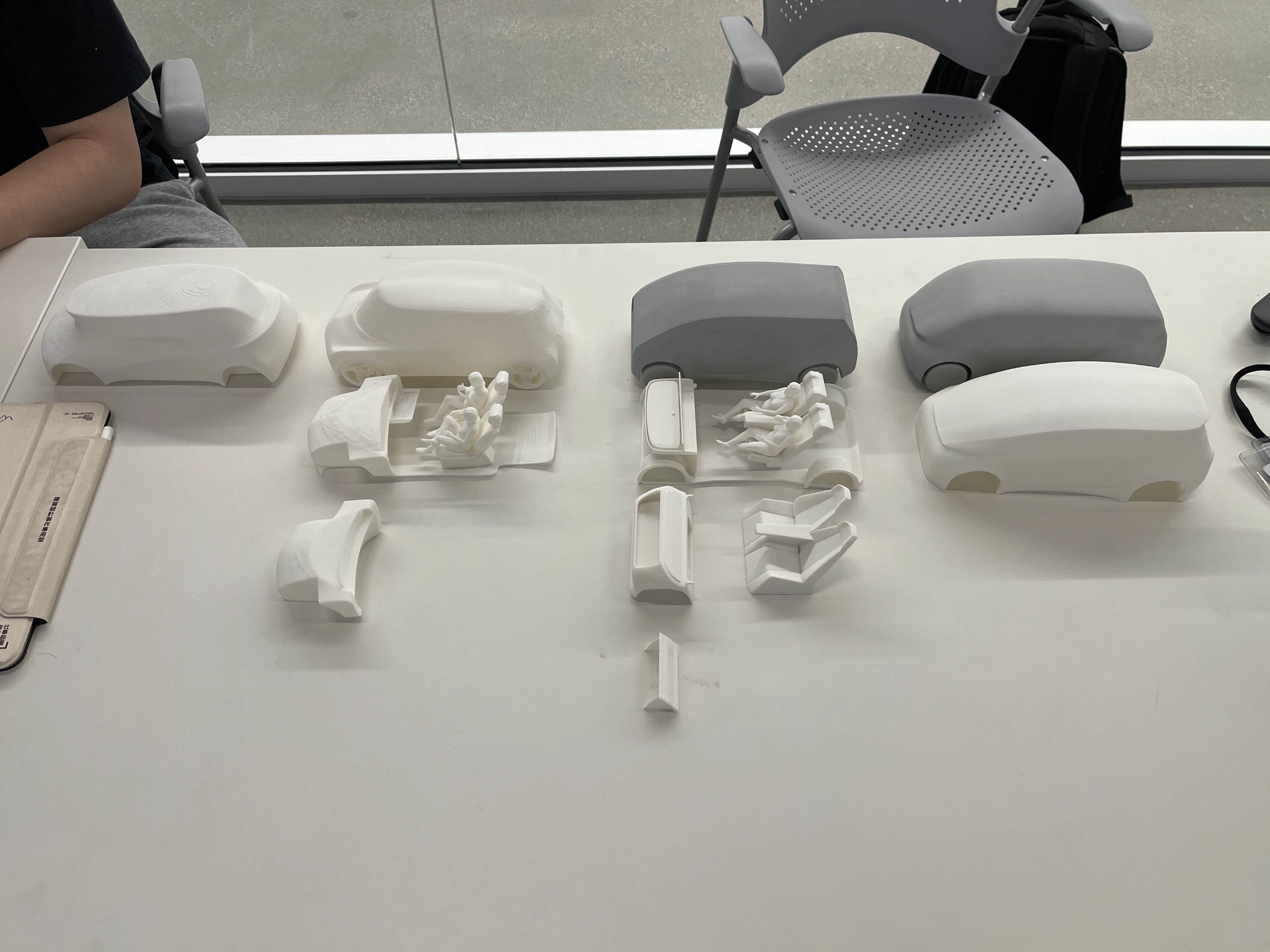 3D printed car models and interior seating arrangements displayed on a white table.