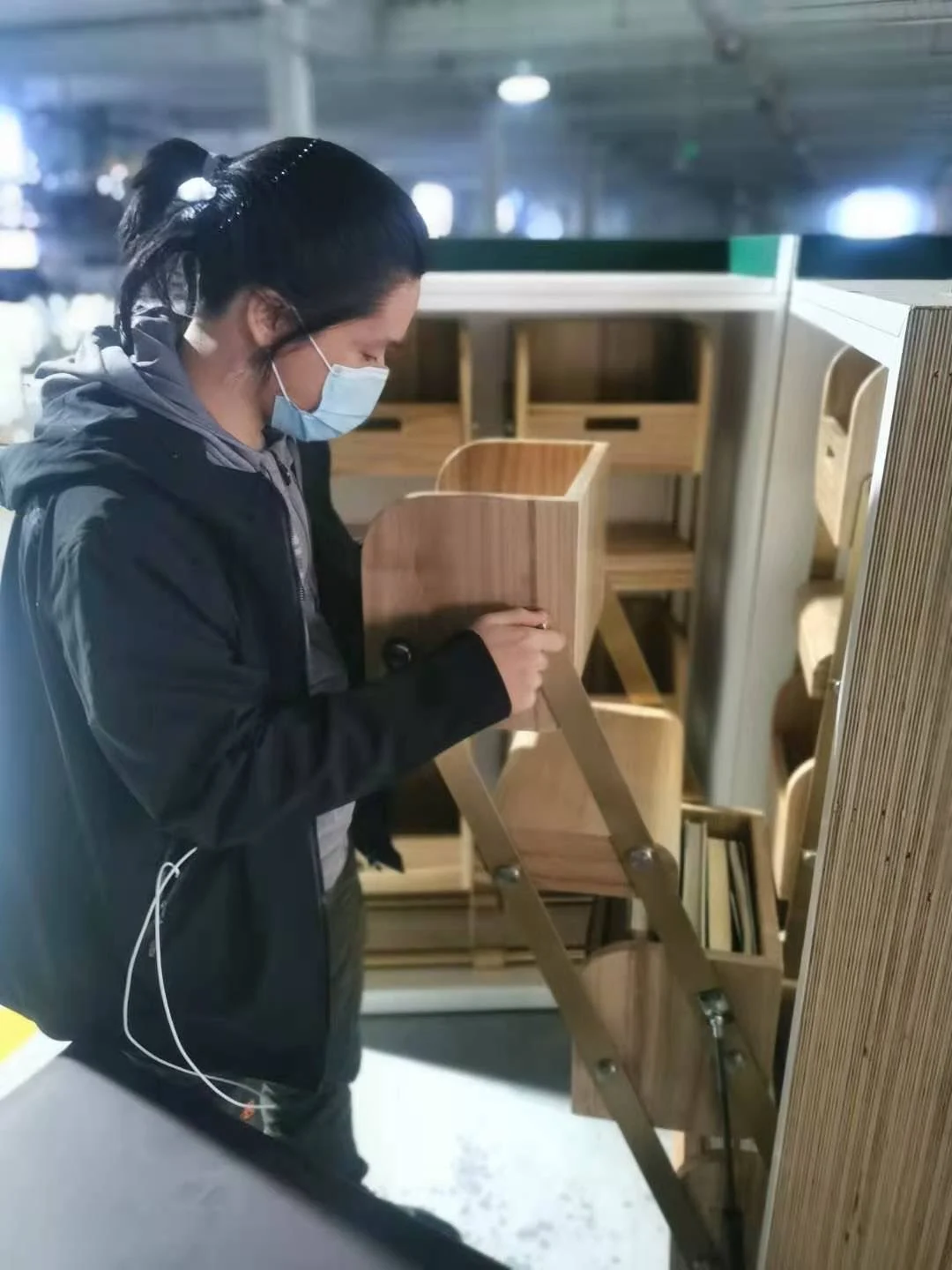 Person wearing a mask adjusts a wooden folding bookshelf with books inside in a well-lit room.