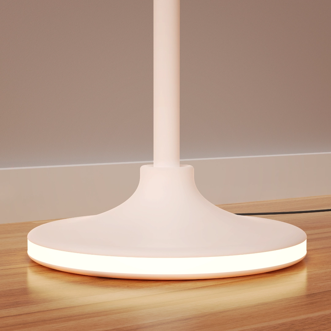 Base of a modern white lamp on a wood surface with a glowing ring of light around the bottom edge.