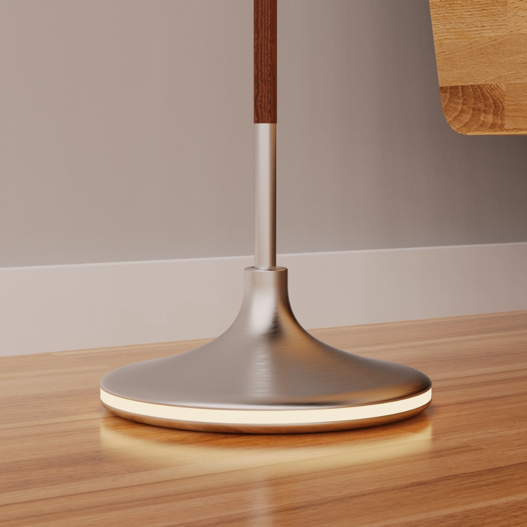 Close-up of a modern metallic lamp base with a glowing ring on a wooden floor by a wall.
