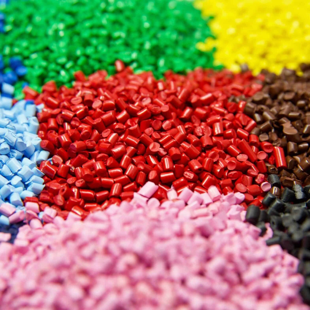 Close-up of colorful plastic pellets in green, yellow, red, brown, black, blue, and pink arranged in groups.