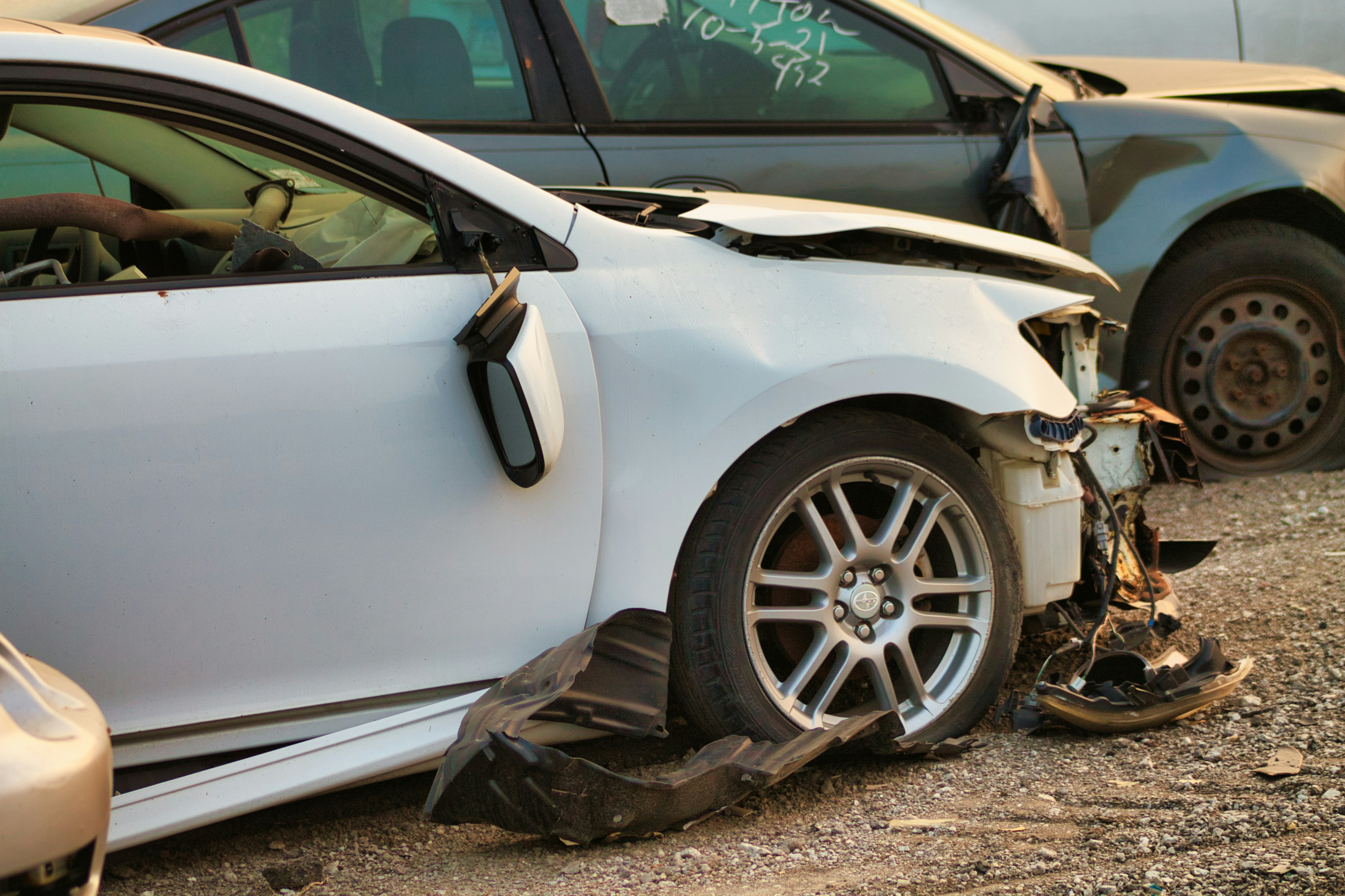 Two badly damaged cars after a crash, with broken parts on the ground.