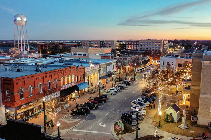 Downtown McKinney at dusk with brick shops, a water tower, and parked cars.