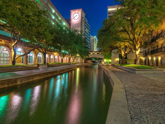The Irving canal walk at night with a clock tower, arched walkways, and lights on the water.