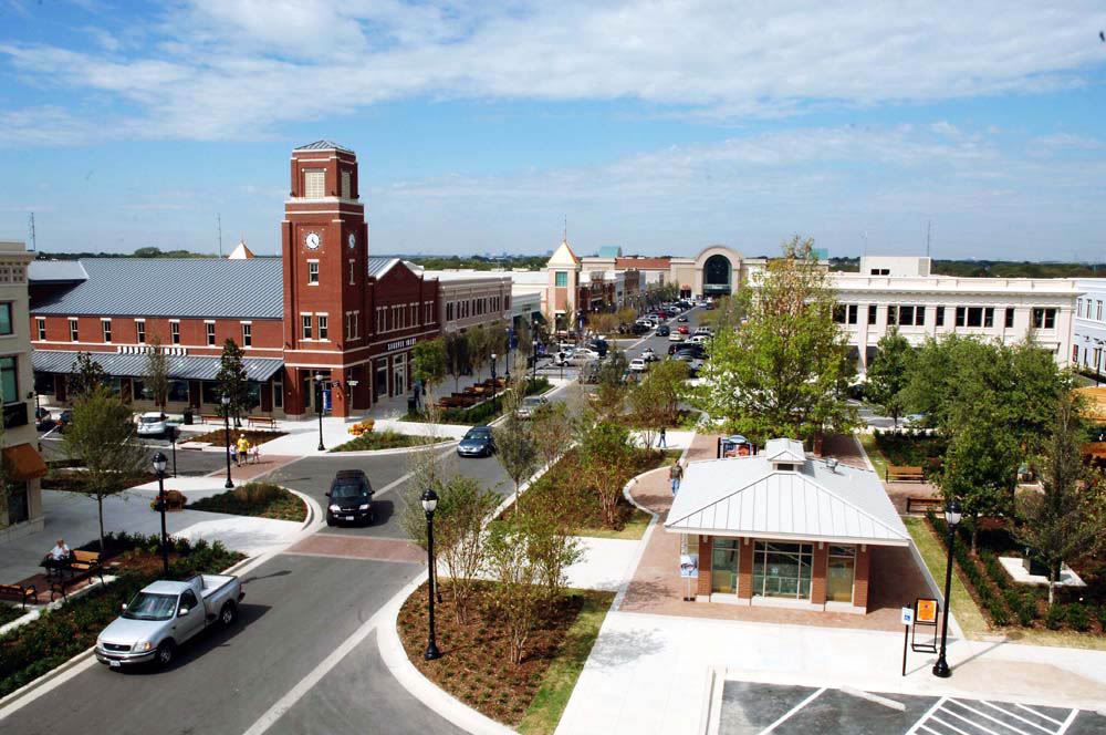 A town square in Grapevine with a brick clock tower, shops, young trees, and cars on the street.