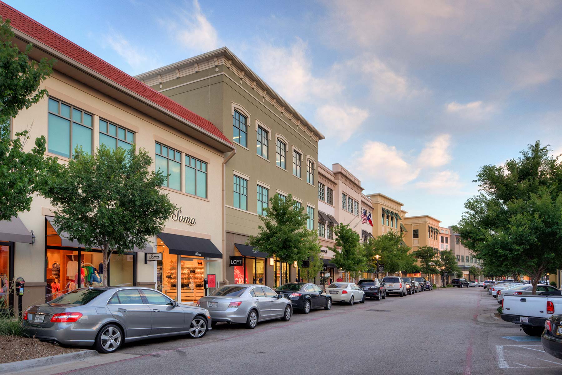A shopping street in Allen with cars parked along the curb and trees on the sidewalk.