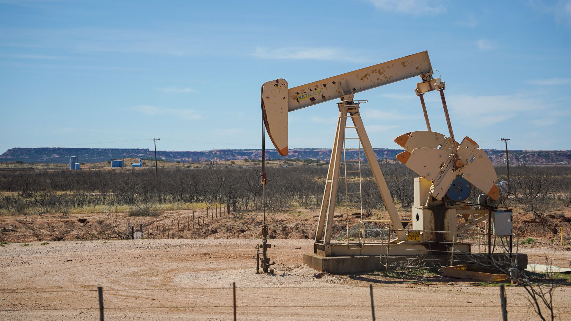 An oil pump jack in a dry field near Midland with low hills in the distance.