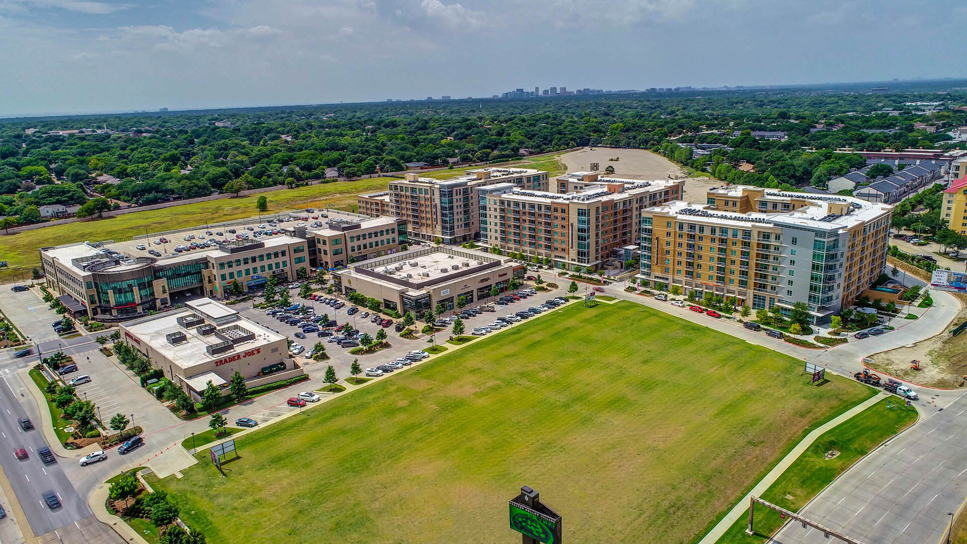 An aerial view of shops, apartments, and green space in Preston Hollow on a sunny day.