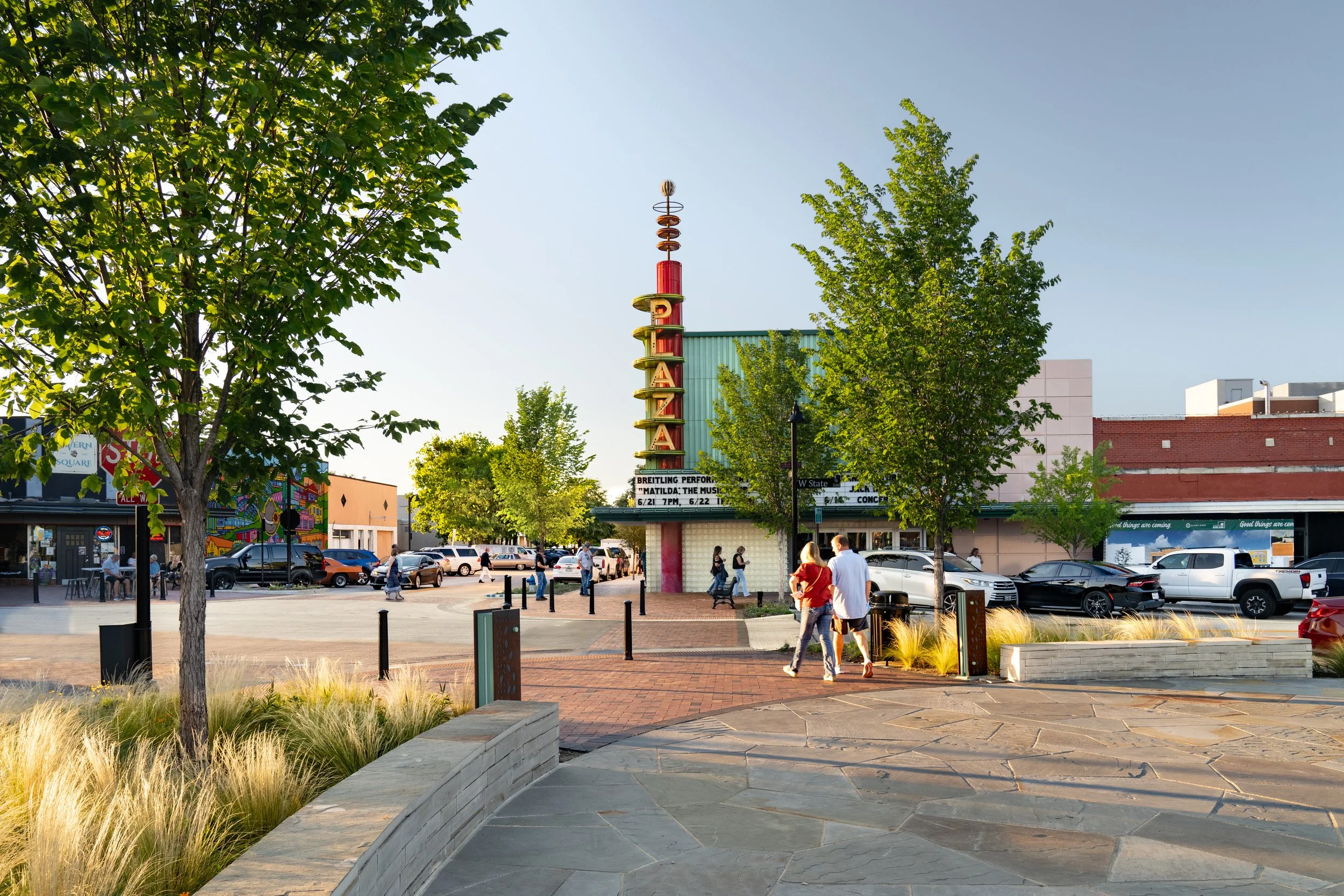 The Plaza Theatre sign in downtown Garland with trees, shops, and people walking nearby.