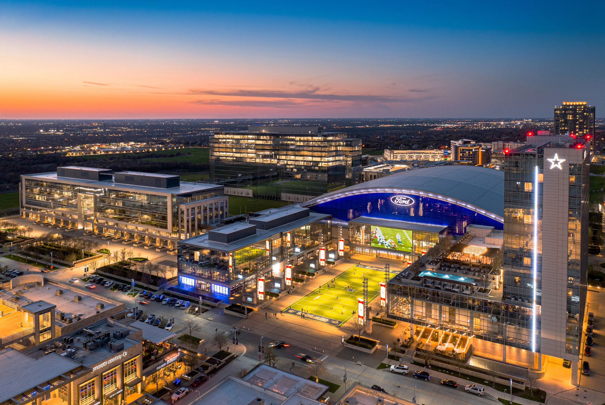 An aerial view of lit up buildings and a stadium in Frisco at sunset.
