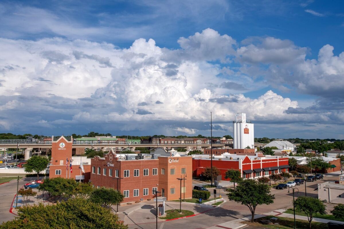 Downtown Carrollton with red brick buildings and tall white grain silos under big clouds.