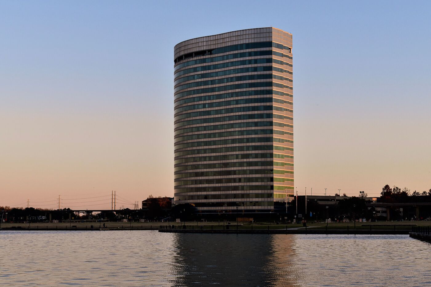 A tall curved glass tower in Irving seen across the water at sunset.