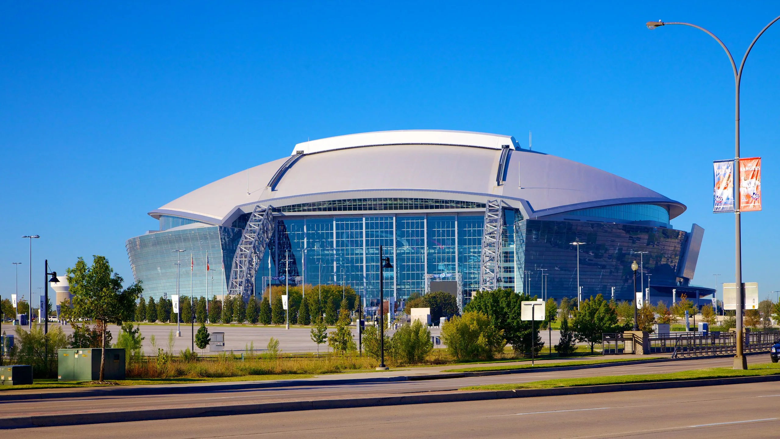A large domed stadium in Arlington with tall glass walls under a clear blue sky.