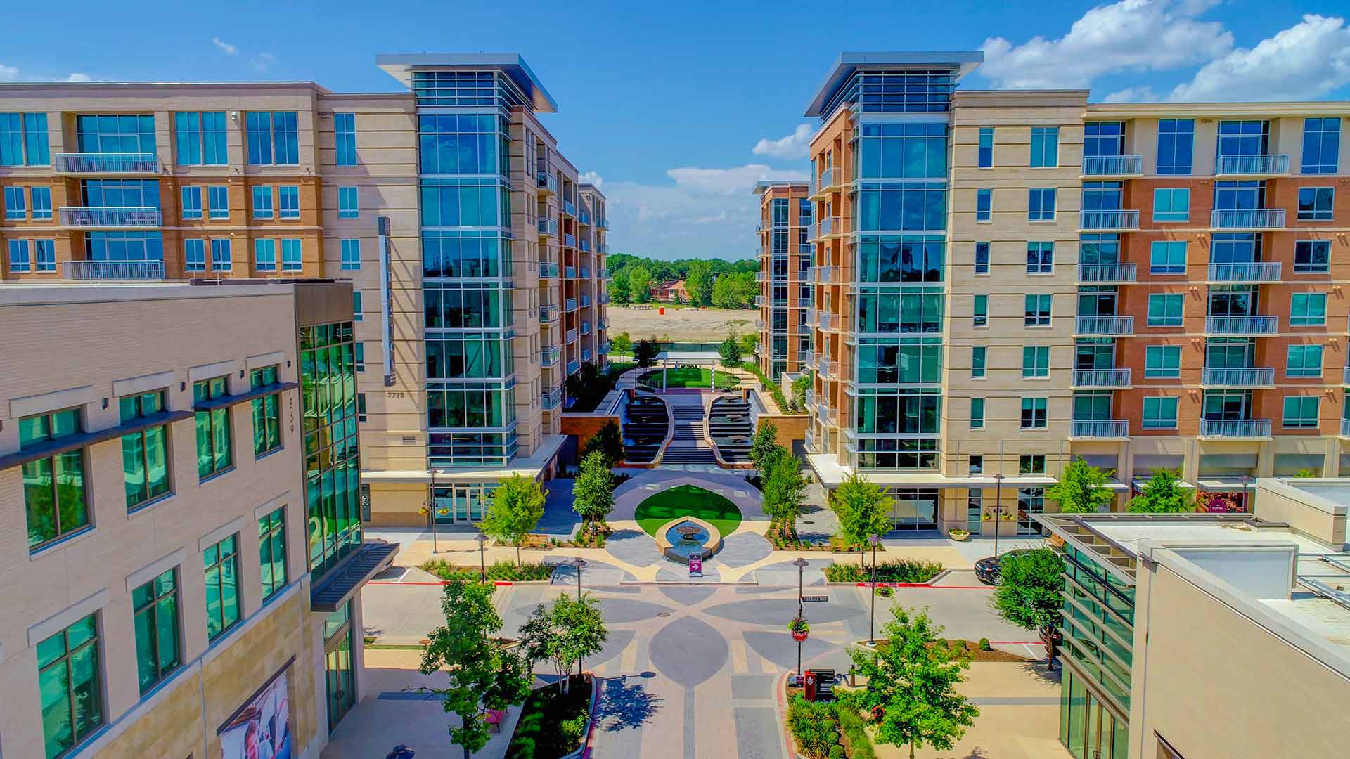 A walkway with trees and a fountain between shops and apartments in Preston Hollow.