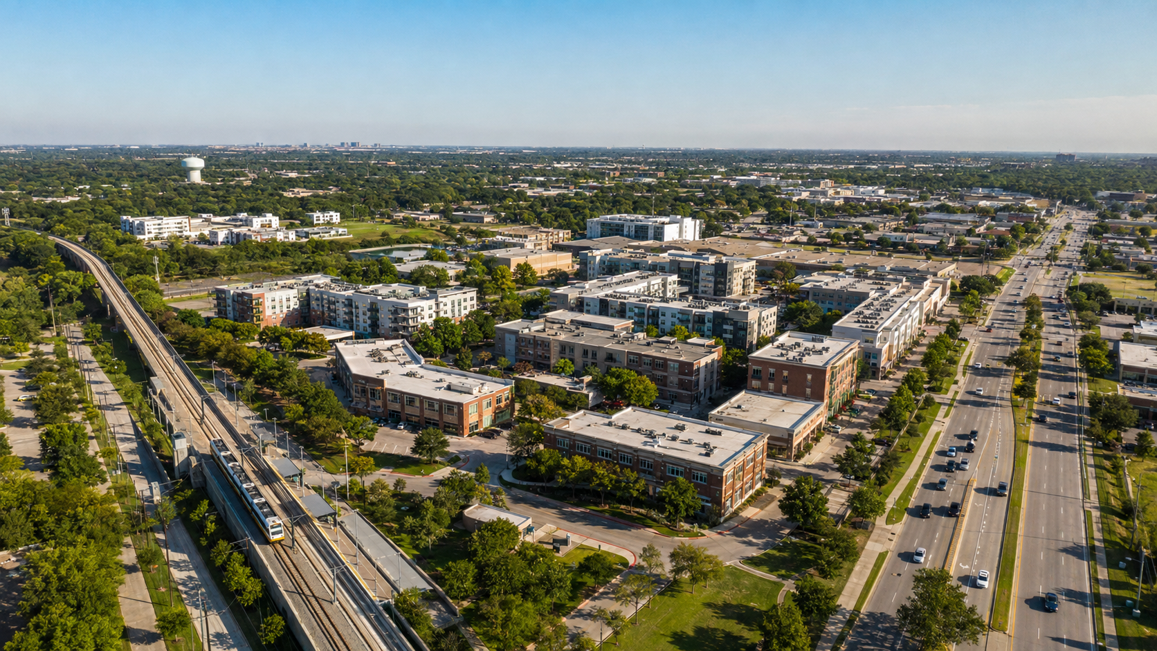 Aerial view of Carrollton with apartment buildings, a train line, and a wide road.