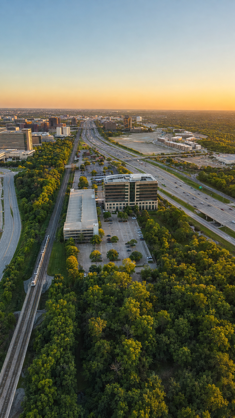 Aerial view of Richardson at sunset with office buildings, a highway, and a train on the tracks.