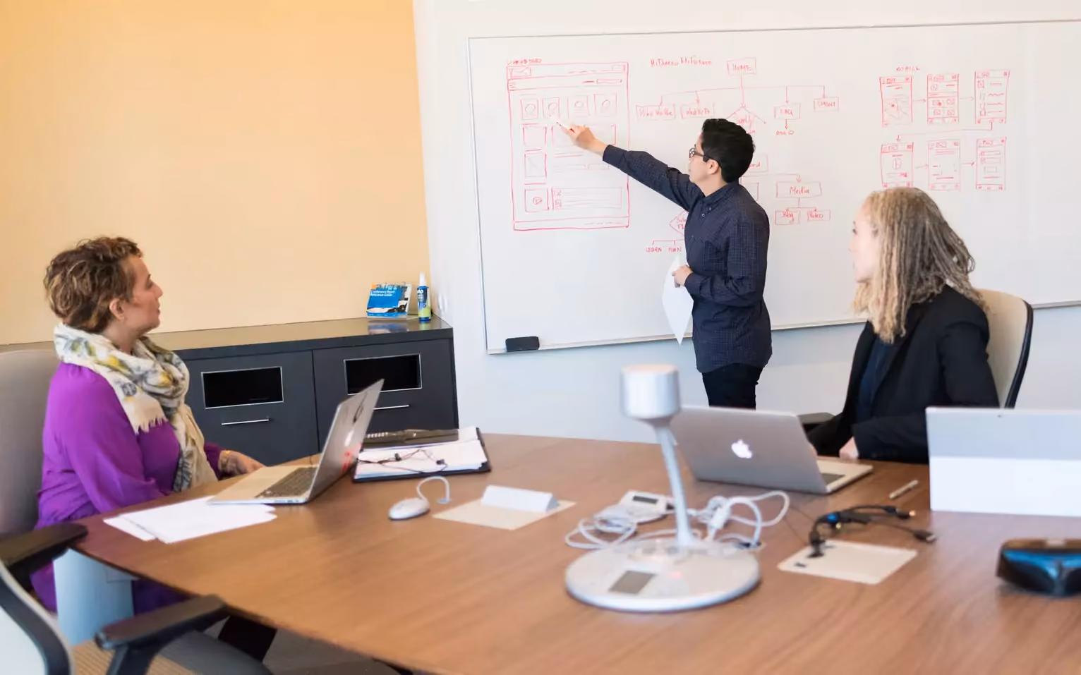 Team meeting in a conference room with a colleague sketching app wireframes on a whiteboard