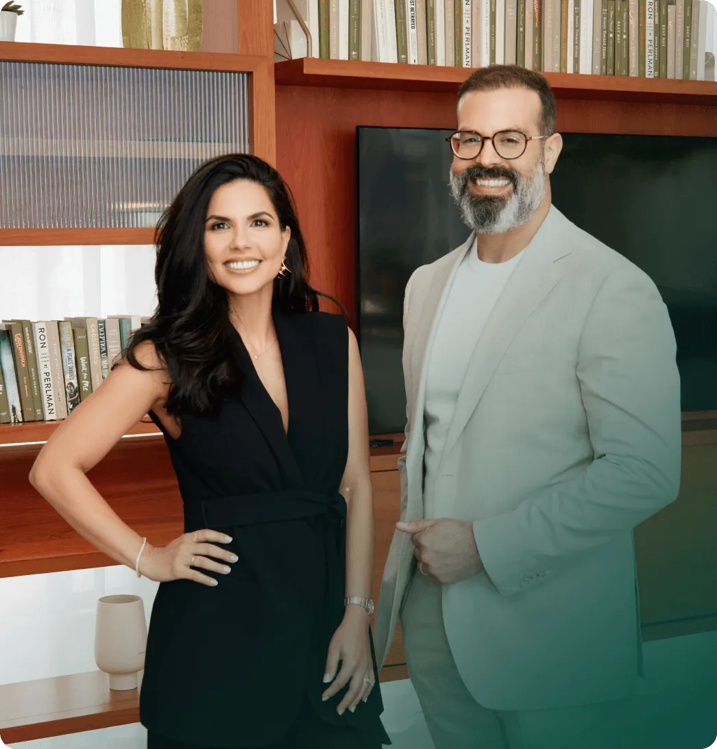 A smiling woman and man standing together in a room with bookshelves and a large screen.