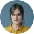 Portrait of a serious woman with dark hair pulled back, wearing a yellow top.