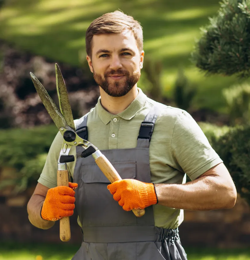 Smiling man in orange gloves holding hedge shears outside in garden.