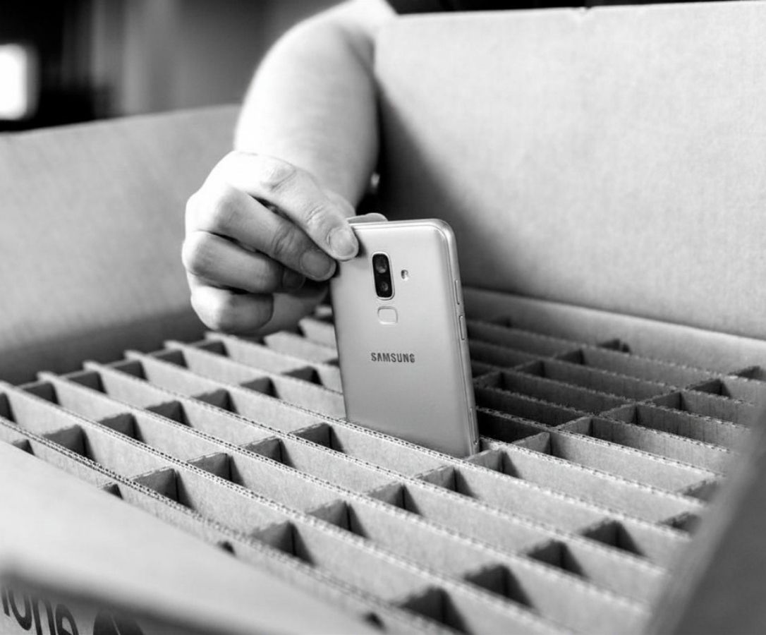 Hand placing a Samsung smartphone upright into a cardboard box with divider slots for packing.