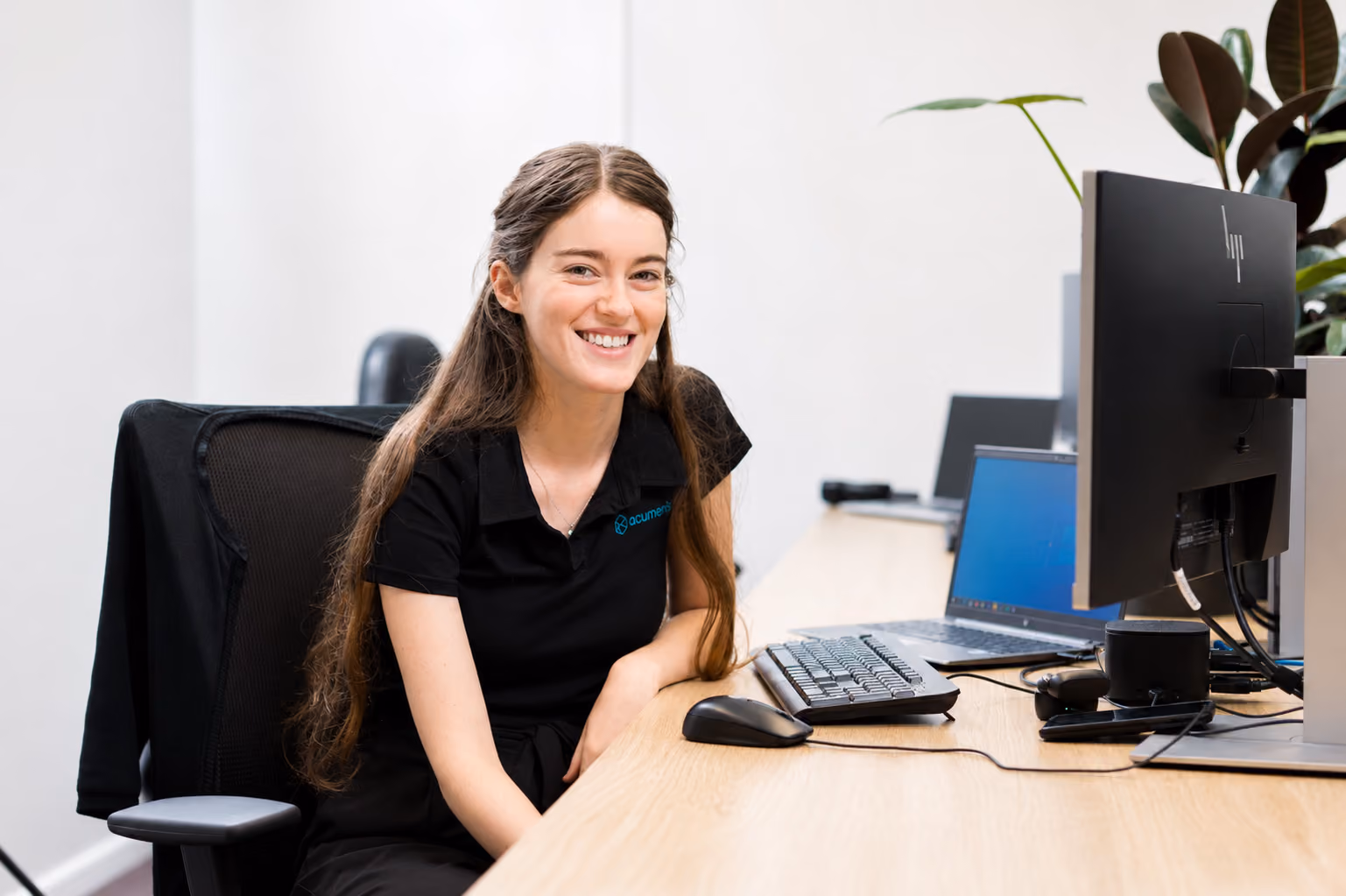Smiling female Australian cyber security consultant with long hair sitting at a desk with a computer.