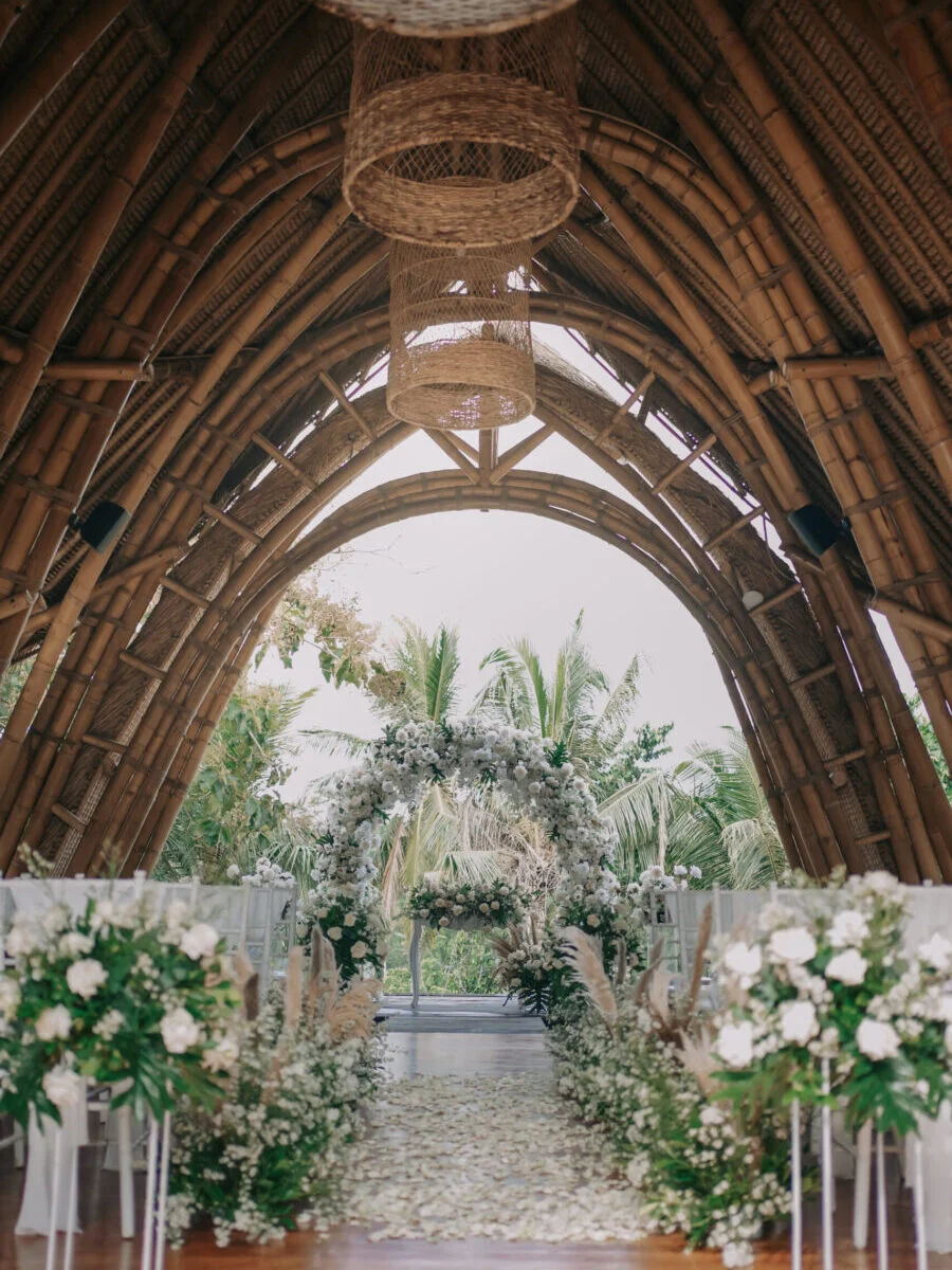 The aisle of the Mantra Pavilion lined with white florals, opening onto the palms beyond