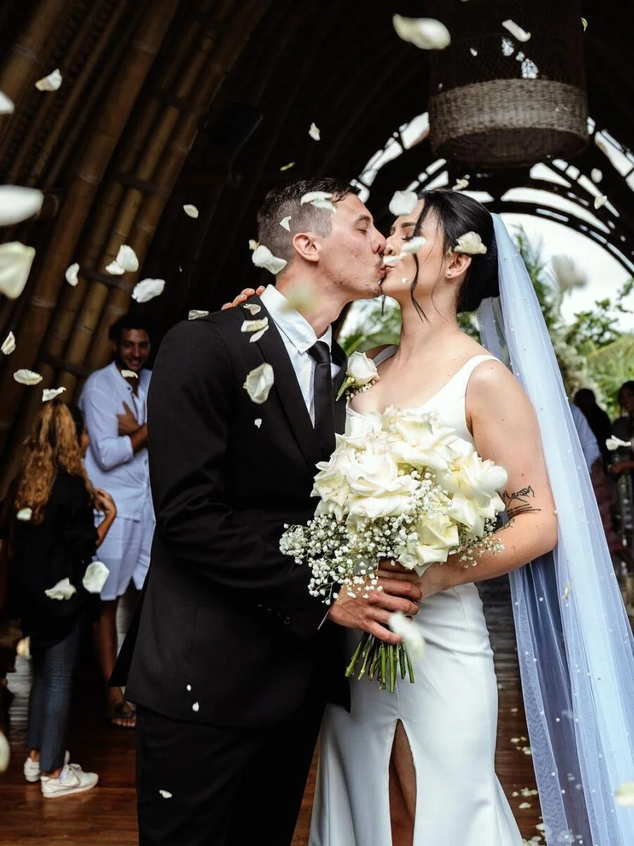 A newly married couple kissing under a shower of white flower petals