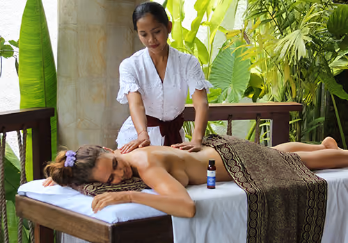 A therapist working along a guest’s back during a Balinese massage, with jungle greenery behind the pavilion