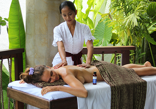 A therapist working along a guest’s back during a Balinese massage, with jungle greenery behind the pavilion