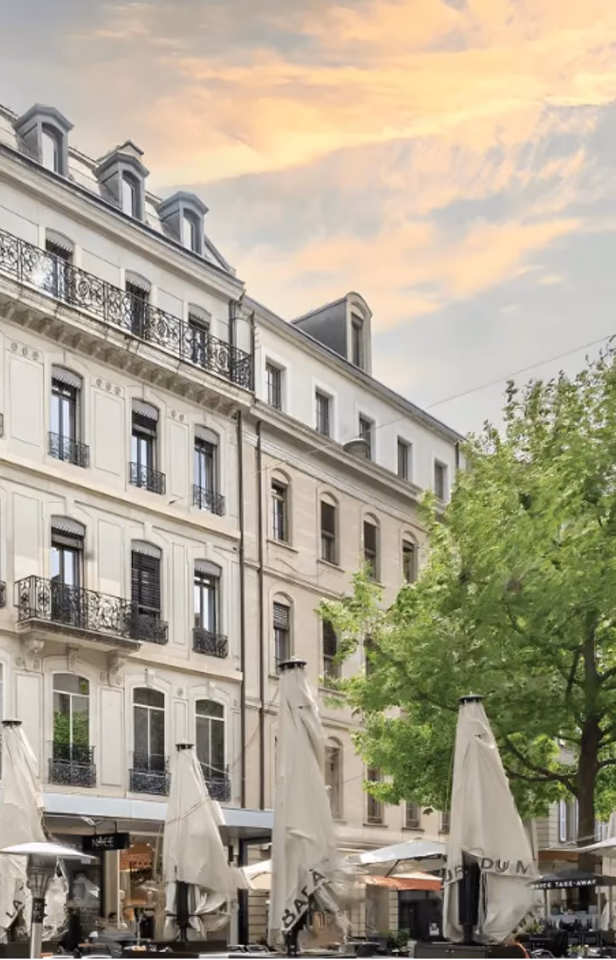 Façade de bâtiments résidentiels européens classiques avec des balcons en fer forgé ornementés et des parasols de café fermés au niveau de la rue.