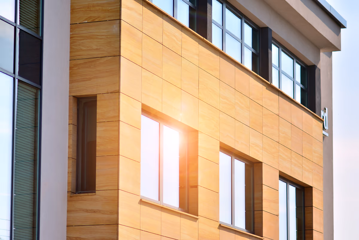 ue rapprochée de la façade extérieure d'un bâtiment moderne en panneaux de bois chaleureux avec de grandes fenêtres reflétant la lumière du soleil.