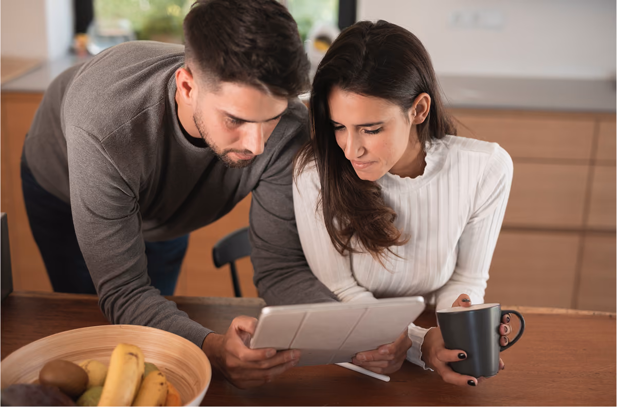 Un homme se penchant au-dessus d'un comptoir en bois pour regarder une tablette numérique avec une femme tenant une tasse de café.