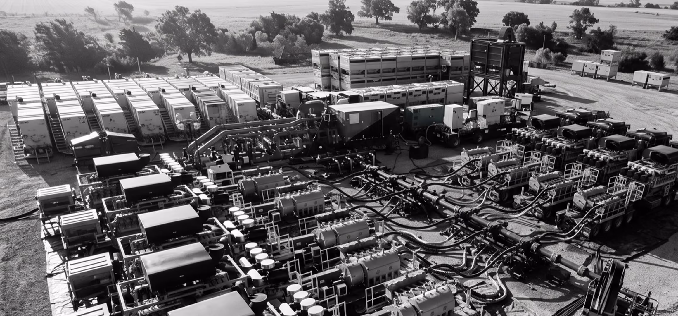 A large industrial site with multiple connected machines and equipment outdoors surrounded by trees.