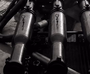 Close-up of three connected metallic hydraulic cylinders with pipes and fittings.