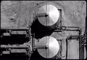 Aerial view of two large round storage tanks with connecting pipes on a concrete surface.