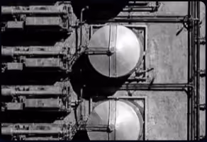 Black and white image of industrial pipes and two large round metallic valves on a wall.