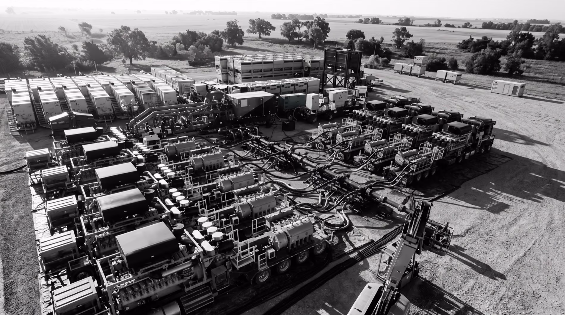 Aerial view of industrial machinery and equipment arranged on a large dirt lot with trees in the background.