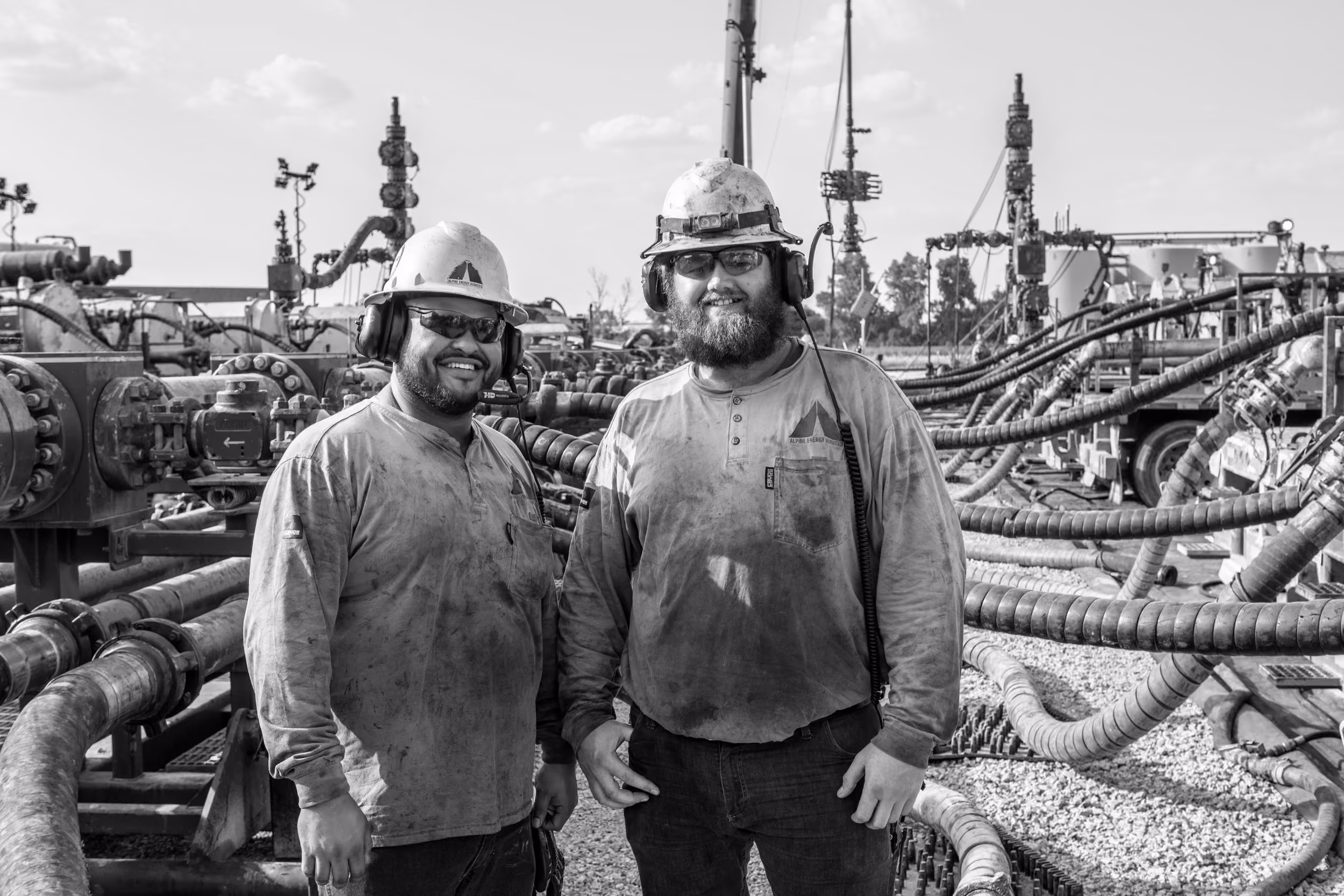 Two Alpine crew members in hard hats smiling on a frac location