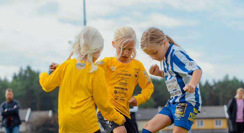 Barn i gule og blå fotballdrakter kjemper om ballen på gresset