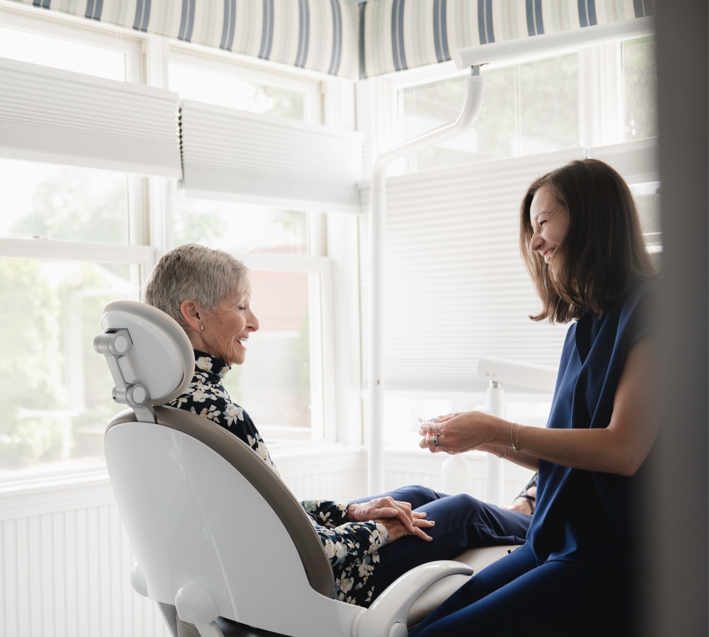 Smiling dental professional showing a dental product to an elderly woman in a dental chair.