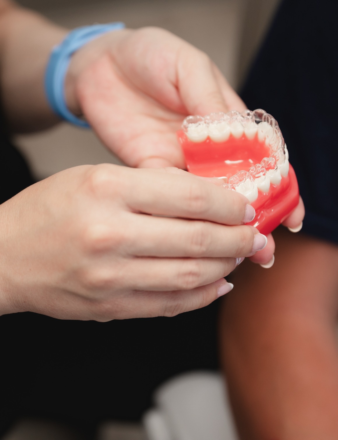 Hands holding a dental model with clear aligners fitted on the upper and lower teeth.