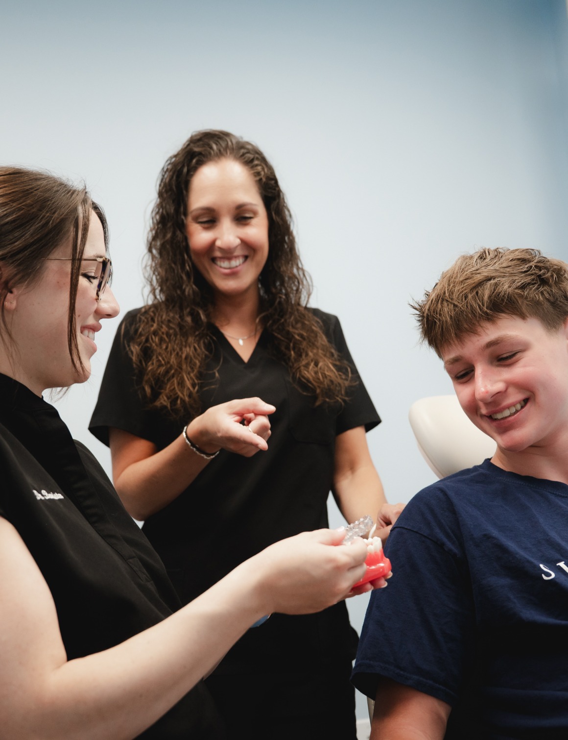 Dental professionals showing a young male patient a teeth model and clear aligner in a dental office.