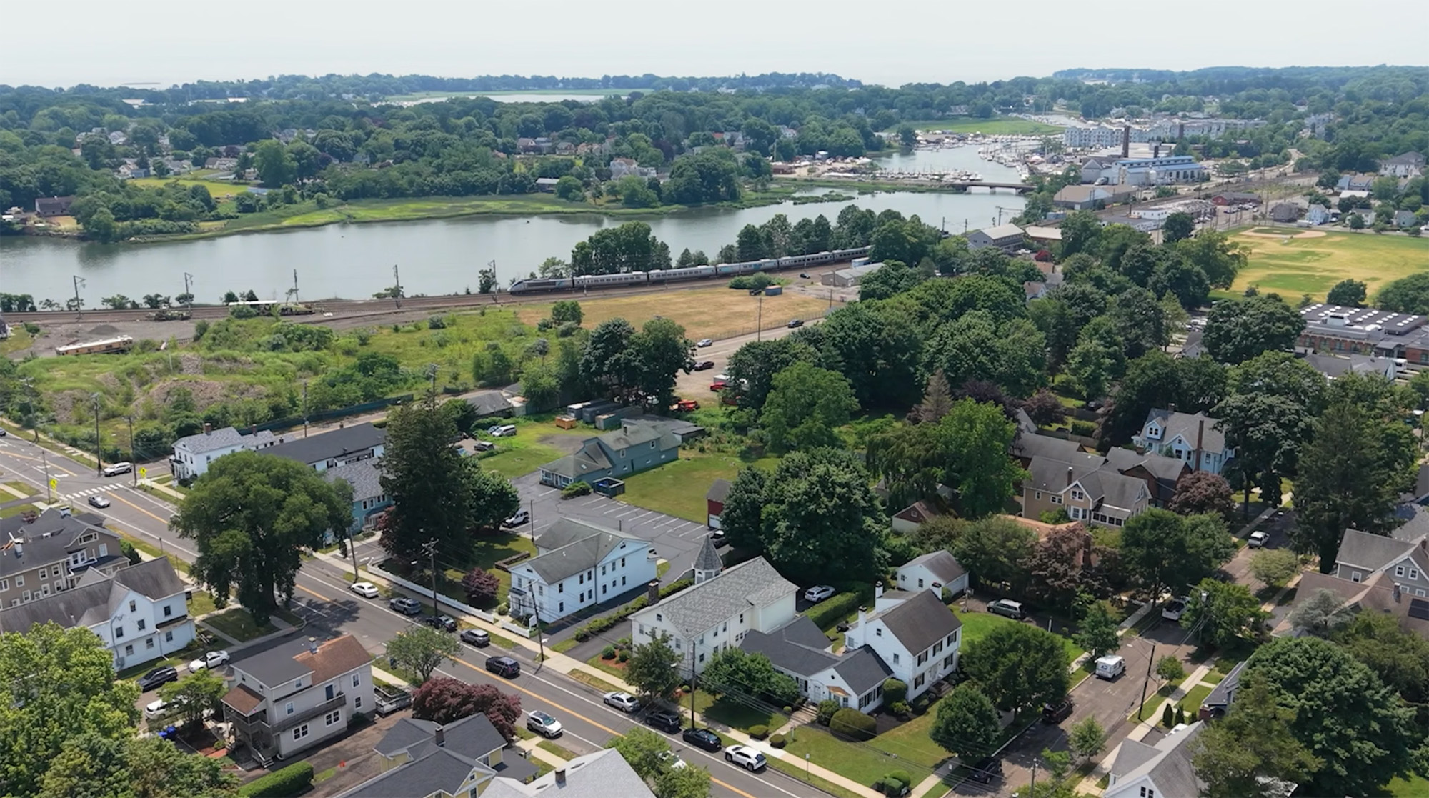 Aerial view of a suburban neighborhood with houses, trees, a river, and a train passing by.
