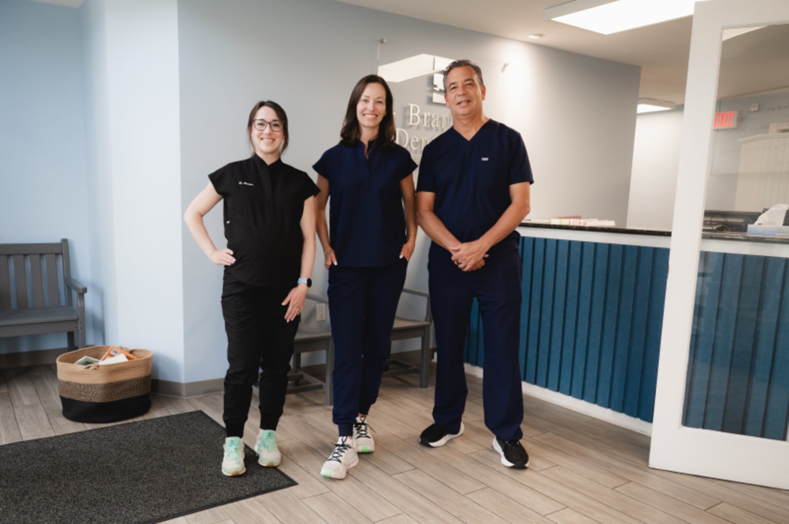Three dental team members smiling together in modern practice setting