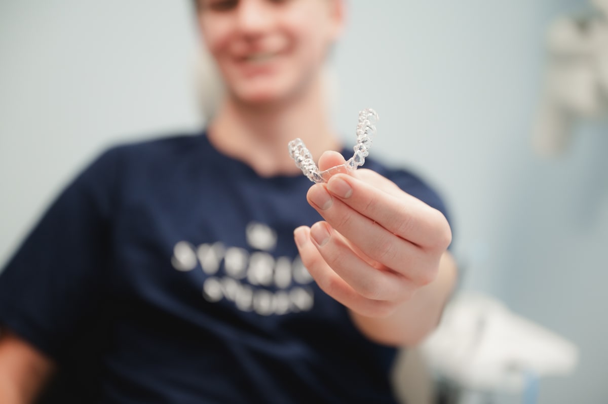 Close-up of clear Invisalign aligner being held between two hands against a neutral background